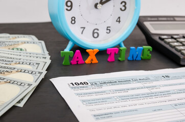 tax form 1040, alarm clock, calculator, dollars and the word "tax time".