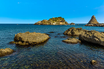 Basalt rocks above and below the sparkling blue sea at Aci Trezza, Sicily in summer