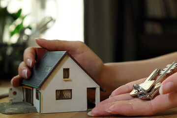 real estate agent holding a miniature house in one hand and keys in the other hand
