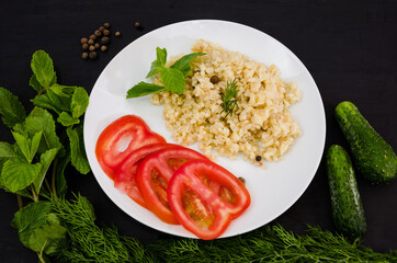 Bulgur, greens and vegetables in a plate on a black table. Tasty and healthy vegetarian food.