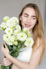 Obraz na płótnie Canvas Cute happy young girl in white blank t-shirt, holding a bouquet and looks at the of flowers, enjoying the smell. beautiful blond teen girl with braces on her teeth smiling