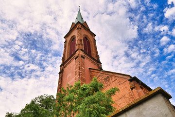 Tower of Protestant church called 'Evangelische Stadtkirche' in front of cloudy blue sky in historical Ladenburg city in Germany