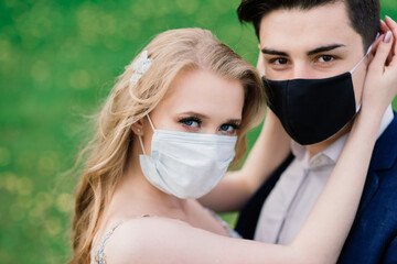 Young loving couple walking in medical masks in the park during quarantine on their wedding day. Coronavirus, disease, protection, sick, illness flu europe celebration canceled.