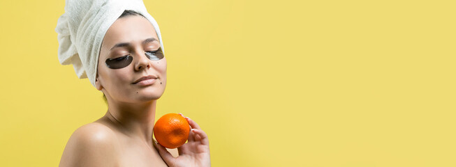 Beauty portrait of woman in white towel on head with gold nourishing mask on face. Skincare cleansing eco organic cosmetic spa relax concept. A girl stands with her back holding an orange mandarin.