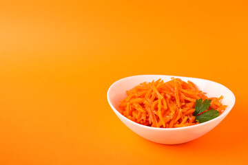 Bowl with carrot salad on orange background, space for text