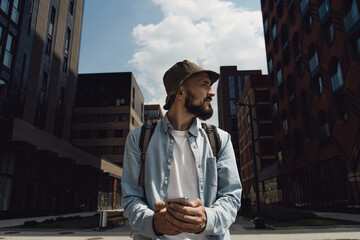 Hiker man in a hat travels around city with a backpack. Traveler stopped to write a message on his...