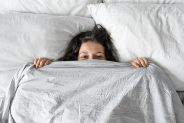 The girl does not want to get out of bed in the morning. Hiding in a blanket. View from above. Ambush in bed