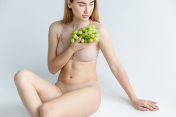 Lady Wearing Beige Swimsuit Model Isolated. Swim Suit Model. Rio Bottoms, Brabrassiere. Girls Briefs. Women Swimming Suit Underwear. Woman holds grapes in the chest and hugs it with both hands.