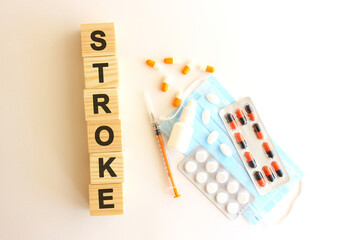 The words STROKE is made of wooden cubes on a white background with medical drugs and medical mask. Medical concept.