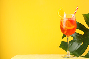 Aperol spritz cocktail and palm leaf on yellow background. Summer drink