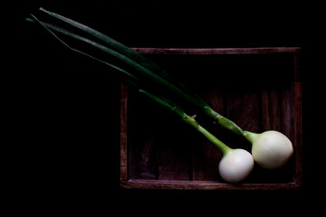 Top view of bunch of green onion with chive in woodden chest on a black background. Bunch of fresh onion and chive on black background. Delicious Fresh vegetables from the garden 