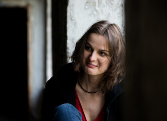 Fototapeta premium Nice color close up portrait of young woman with emotions on face behind the window in day light in abandoned house
