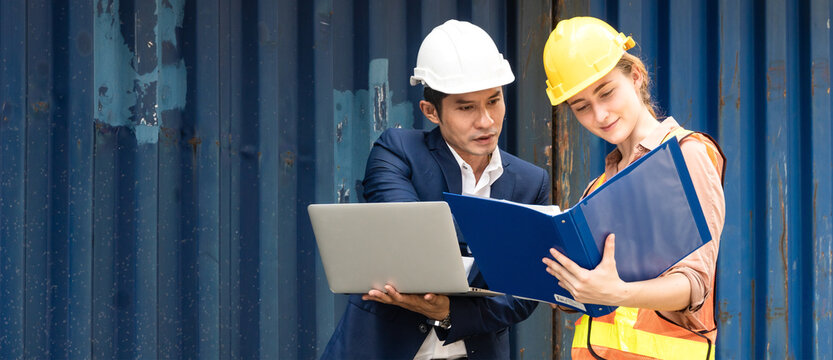 Asian man logistic warehouse foreman using laptop checking list of container boxes from cargo with woman worker working on document. import export shipping business. planning and strategy. copy space