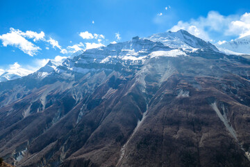 Fototapeta premium A panoramic view on sharp and dangerous, high, snow capped Himalayan peaks long Annapurna Circuit in Nepal. Slopes are overgrown with small bushes. Exploration and discovering. Steep mountain wall.