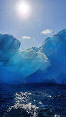 Sun high up above glacial blue iceberg in antarctic sea 