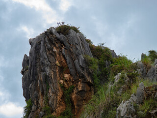 Crag with vegetation under a cloudy, blue sky