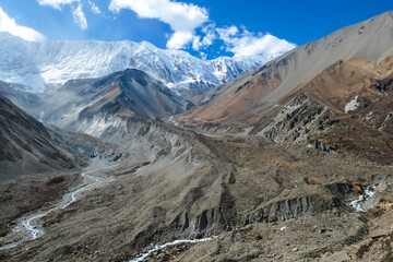 Fototapeta na wymiar A panoramic view on a valley along Annapurna Circuit in Nepal. In the back there are high, snow capped Himalayan peaks. Slopes are overgrown with small bushes. Exploration and discovering