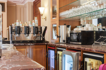 Close-up of empty marble vintage coffee bar counter with coffee machine, microwave oven, glasses shelves and blue light fridges.