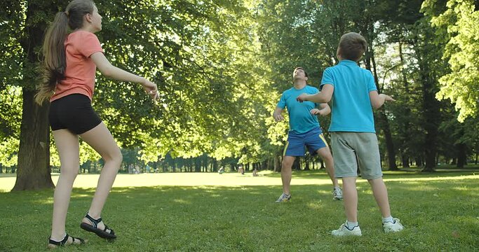 Father and children play in volleyball, Father's day, Playful Man teaching son and daughter volleyball outdoors in sunny day at public park. Family sports weekend. 4K video