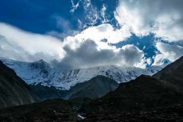 Obraz premium A close up view on high, snow capped Himalayan peaks along Annapurna Circuit in Nepal. Barren and sharp slopes. Mountains are partially shrouded with clouds. Exploration and discovering new places