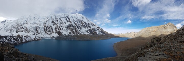 Naklejka premium A panoramic view on turquoise colored Tilicho lake in Himalayas, Manang region in Nepal. The world's highest altitude lake (4949m). Snow capped mountains around. Calm surface of the lake. Serenity