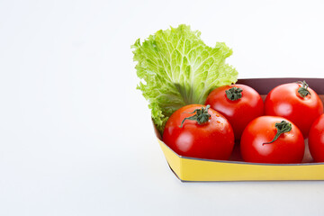Red juicy tomatoes in an eco friendly packaging or container decorated with a leaf of lettuce on a white isolated background. The concept of eco-friendly packaging and organic products. Space for text