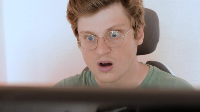 Portrait of young caucasian man with glasses works at the computer and unexpectedly something goes wrong that makes him angry and disappointed