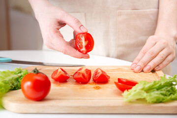 Female hands cut a juicy red tomato into quarters or slices with a knife on a wooden cutting board. A method of preparing vegetables and ingredients before cooking