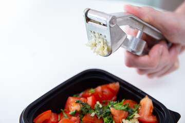 Salsa dip. Juicy red sliced tomatoes with herbs, lemon and garlic. Home cooking. Fresh ingredients or vegetables for salsa sauce. Male hands hold a garlic press or garlic squeezer