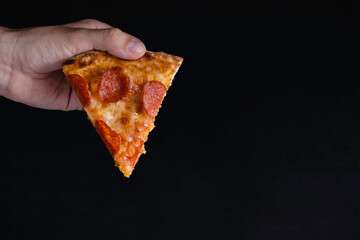 Slice of new york style pizza with pepperoni isolated black background. The concept of fast food.
