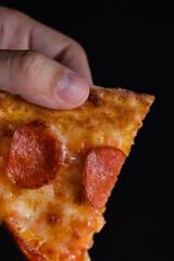 Slice of new york style pizza with pepperoni isolated black background. The concept of fast food. Close up