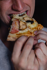 Close up portrait of excited happy hungry young man eating a piece of pizza, focus pizza. Young caucasian man eating pizza