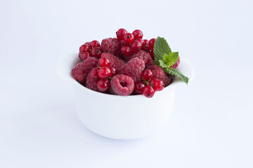 Raspberry and red currant in the white bowl on the white background. Closeup.