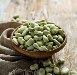 Fresh broad beans in a ceramic bowl on a wooden table