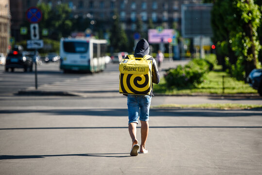 Russia, Saint Petersburg, June 26, 2020: Courier boy in an empty city with a bag "Yandex Food" on his back, view from the back