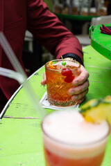 Freshly made orange whiskey cocktail with cherries with another cocktail in front of it