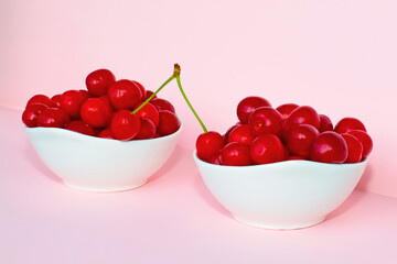 Cherry berries in two bowls on a pink background. Two cherries in one branch - one in one bowl, the second on the other. Two cherries on a branch connect two bowls. Summer concept