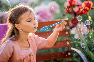 girl blows soap bubbles on the background of flowers in the garden