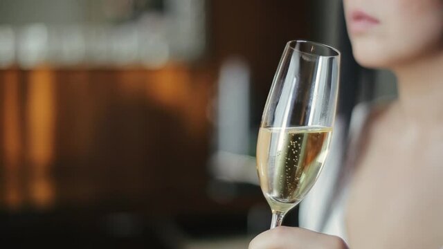 Close-up side view of a glass of champagne in the hands of a pretty bride, in which air bubbles rise up. Caucasian bride holds a glass of champagne in her hand and says something in the hotel room.