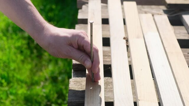 Hammering a big thick nail into wooden board close-up