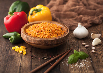 Wooden bowl with long grain basmati rice with vegetables on wooden table background with sticks and paprika pepper with corn,garlic and basil.