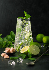 Luxury glass of Mojito cocktail with ice cubes,mint and lime on black board with spoon and fresh limes with cane sugar.