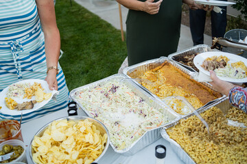 overhead view of people serving buffet food in disposable chafing dishes at backyard dinner event	