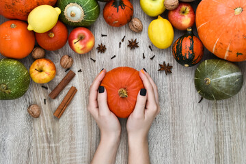 Female hands hold a pumpkin on a background of autumn. Autumn background from pumpkins and fruits on a wooden background. Autumn background concept. Pumpkin, apples, lemon, nuts