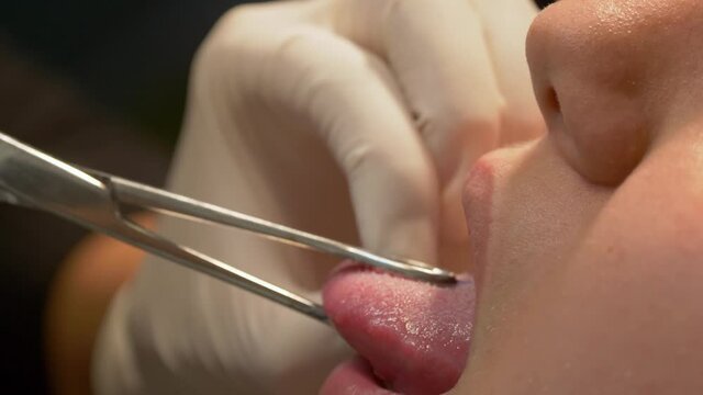 Piercing the tongue in close up view at a professional piercing and tattoo studio
