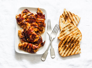 Delicious - roasted bbq chicken breast wrapped in ham, grilled bread on a light background, top view