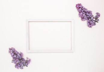 White wooden frame on a white background and lilac flowers. Free space for text, mockup.