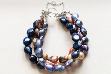 handcrafted bracelet from colored natural river pearls and silver clasp close up on pale wooden board