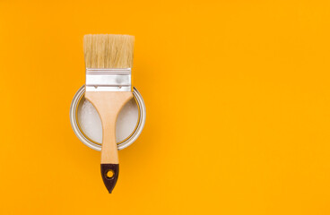 Paintbrush with a wooden handle on a metal can with paint on a yellow background, sitting on top....