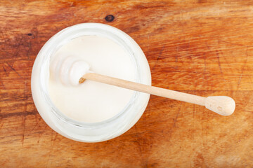 top view of honey spoon in glass jar with natural organic white honey on wooden board